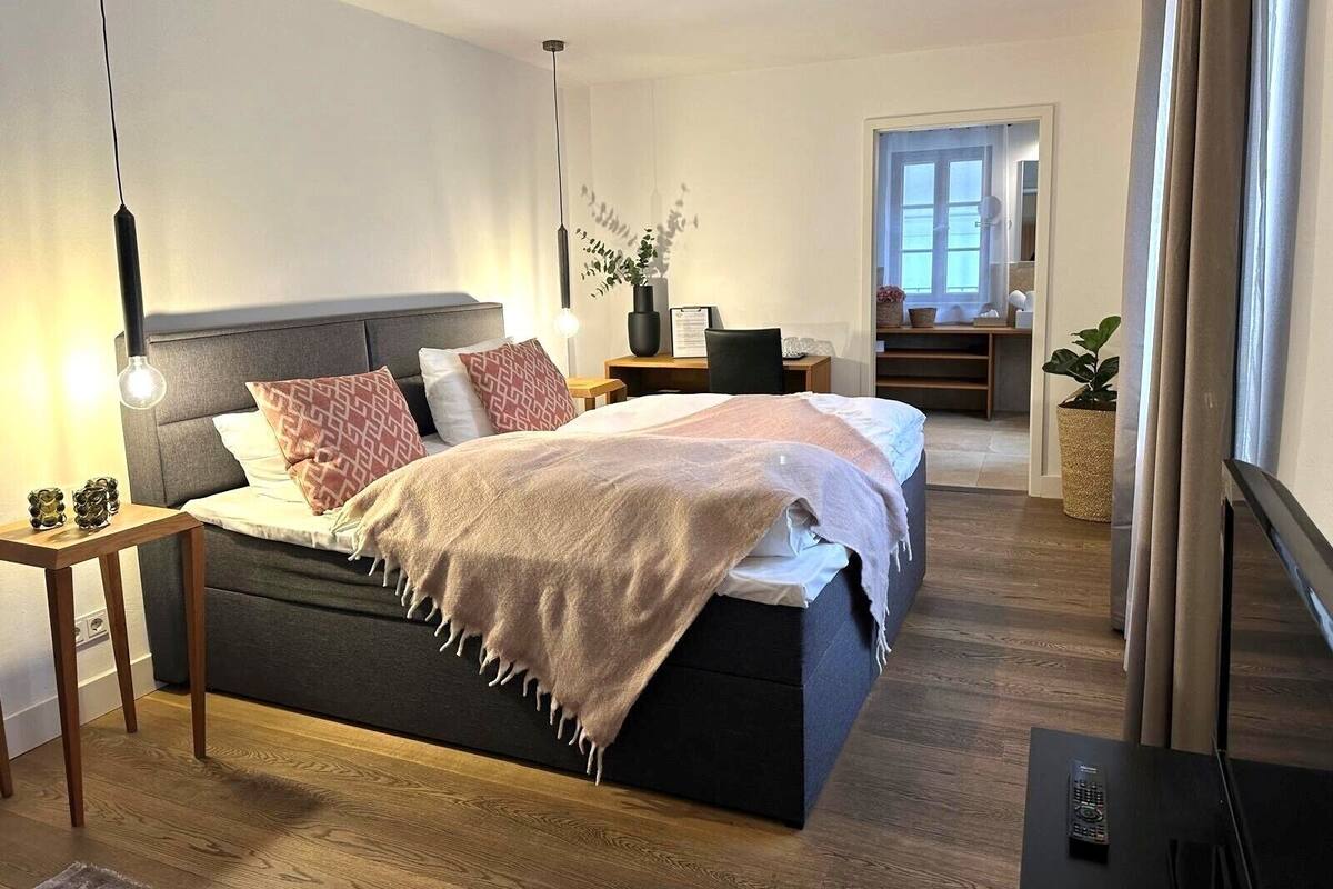 A modern bedroom with a bed, bedside table, lamp, and a view of a balcony.