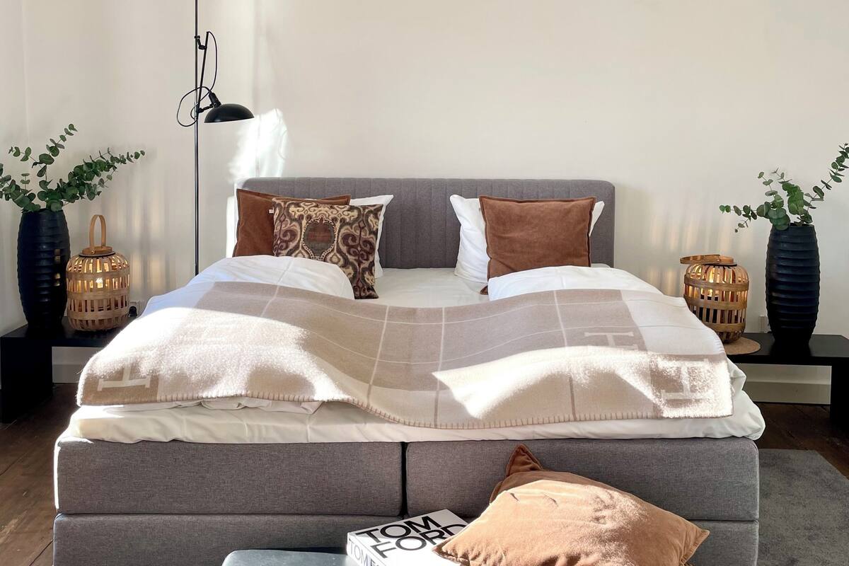 A neatly arranged bedroom with a bed, bedside tables, and a reading chair.