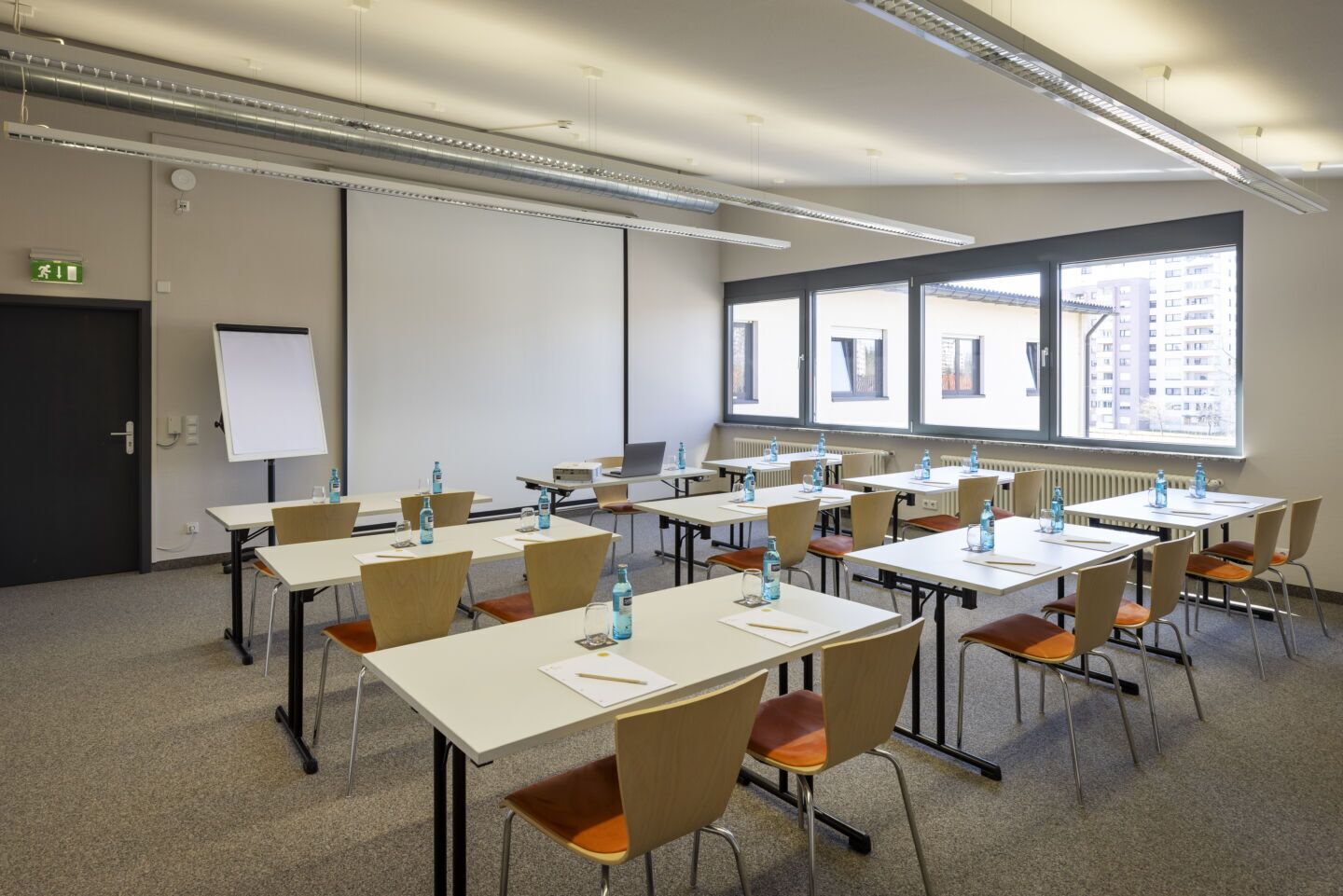 A conference room with tables, chairs, a whiteboard, and a projector screen.