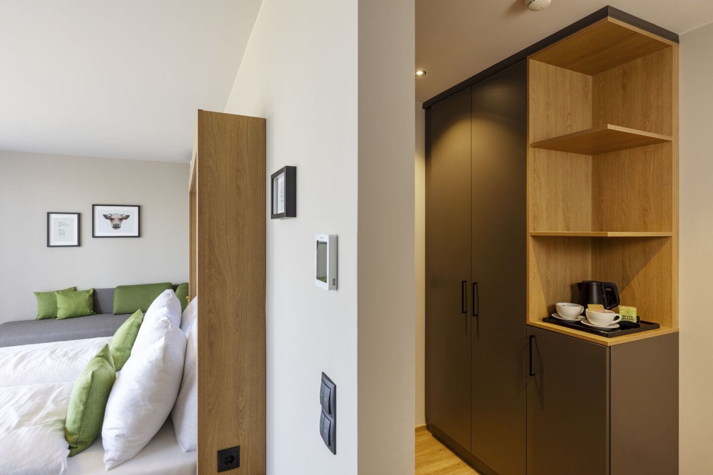 Un dormitorio moderno con una cama, almohadas verdes, un armario de madera y un estante con una cafetera.