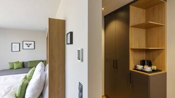 Un dormitorio moderno con una cama, almohadas verdes, un armario de madera y un estante con una cafetera.