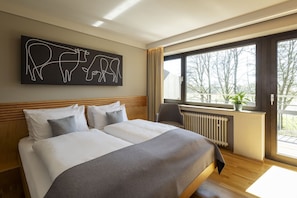 A hotel room with a large bed, a window with a view of trees, and a wall art piece of animals. - JUFA Hotel Wangen im Allgäu (Wangen im Allgäu)