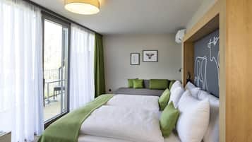 A modern bedroom with a large bed, green and white bedding, a grey sofa, and a view of a balcony.