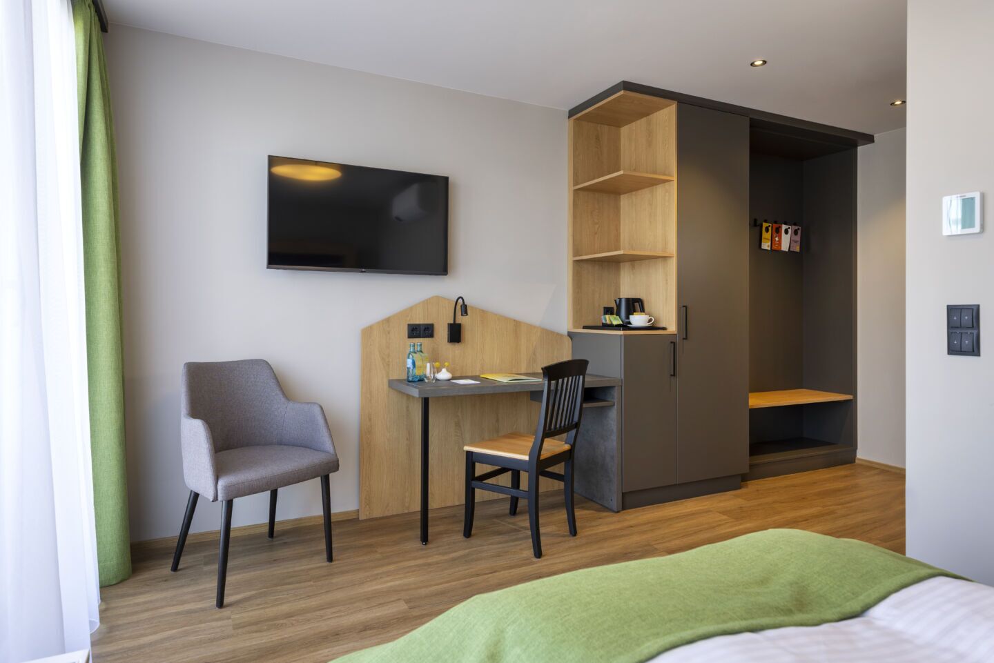 Et moderne hotelværelse med seng, skrivebord, stol, fjernsyn og garderobeskab.