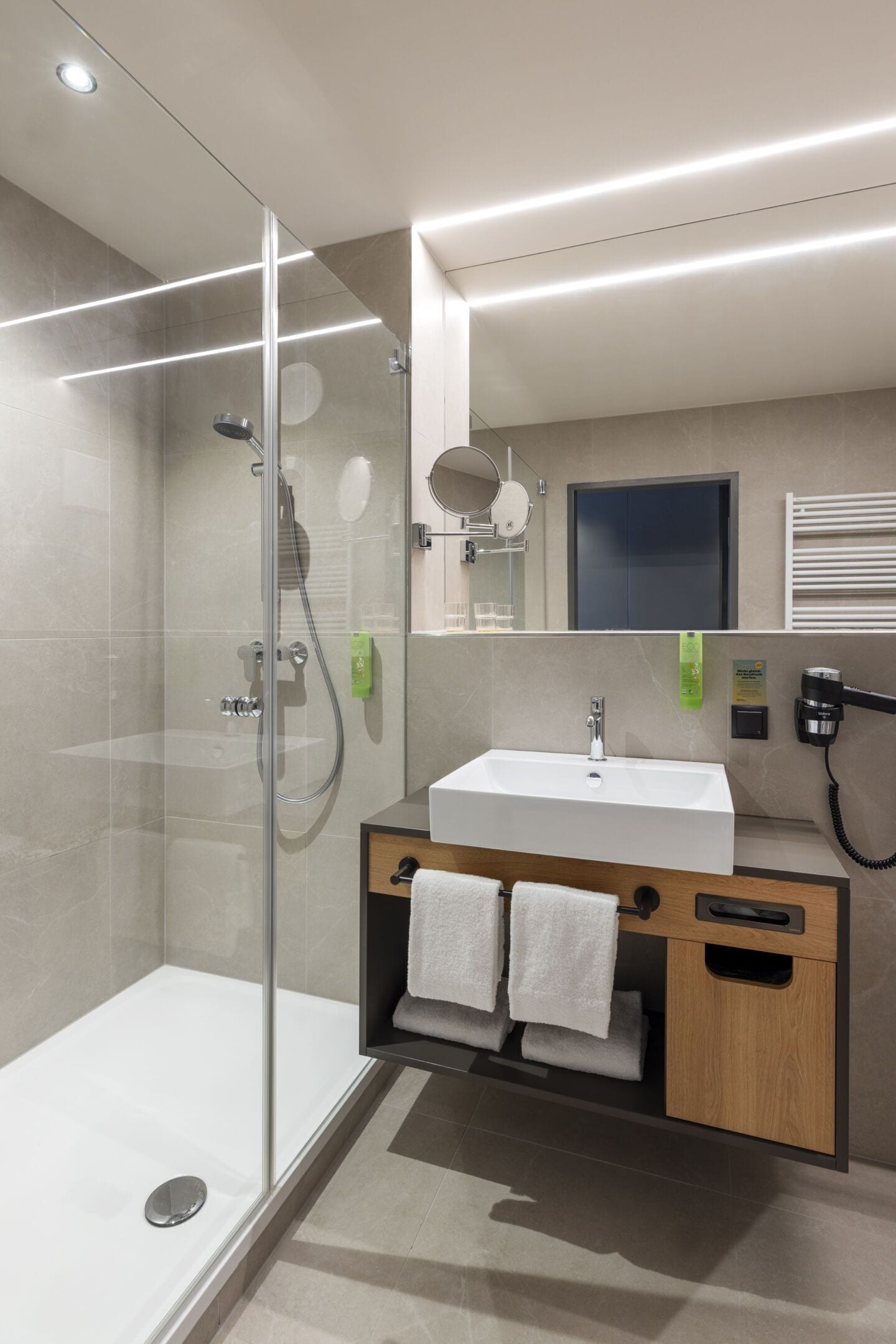 A modern bathroom with a glass-enclosed shower, a white sink, and a wooden vanity.