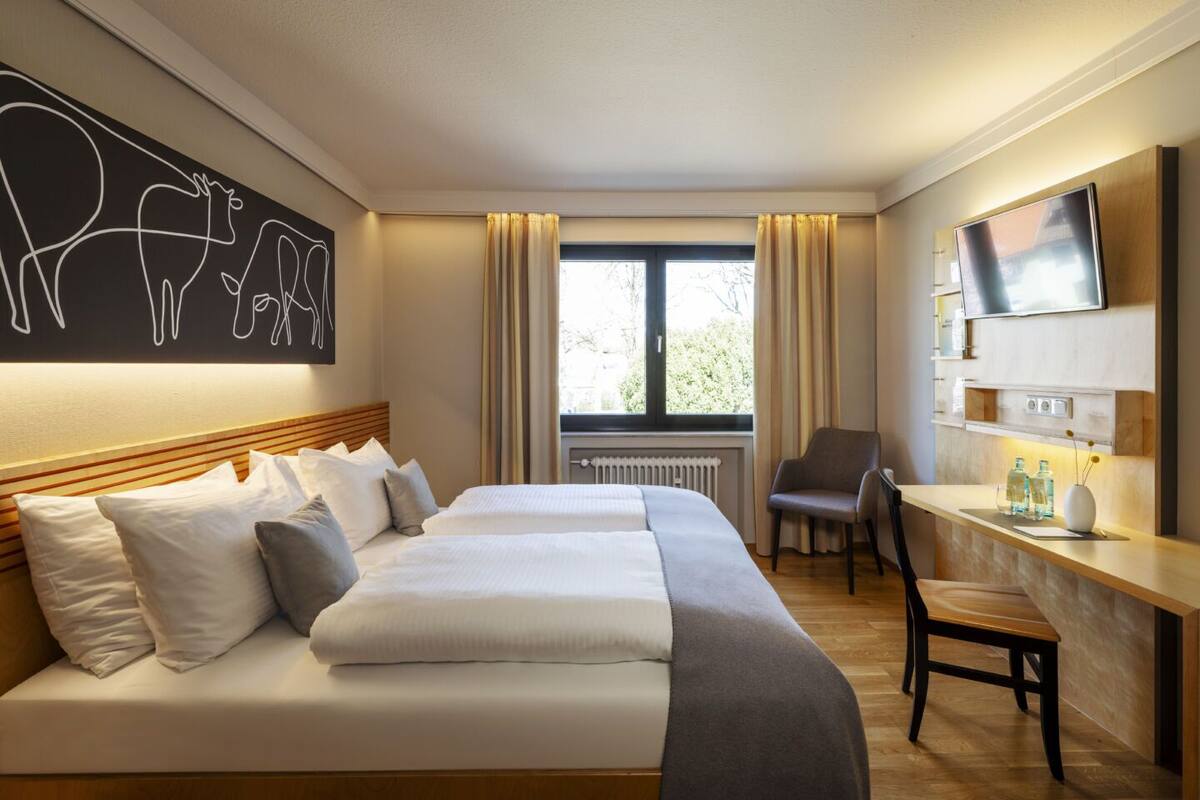 A hotel room with a large bed, a desk, a chair, a TV, and a window with curtains.