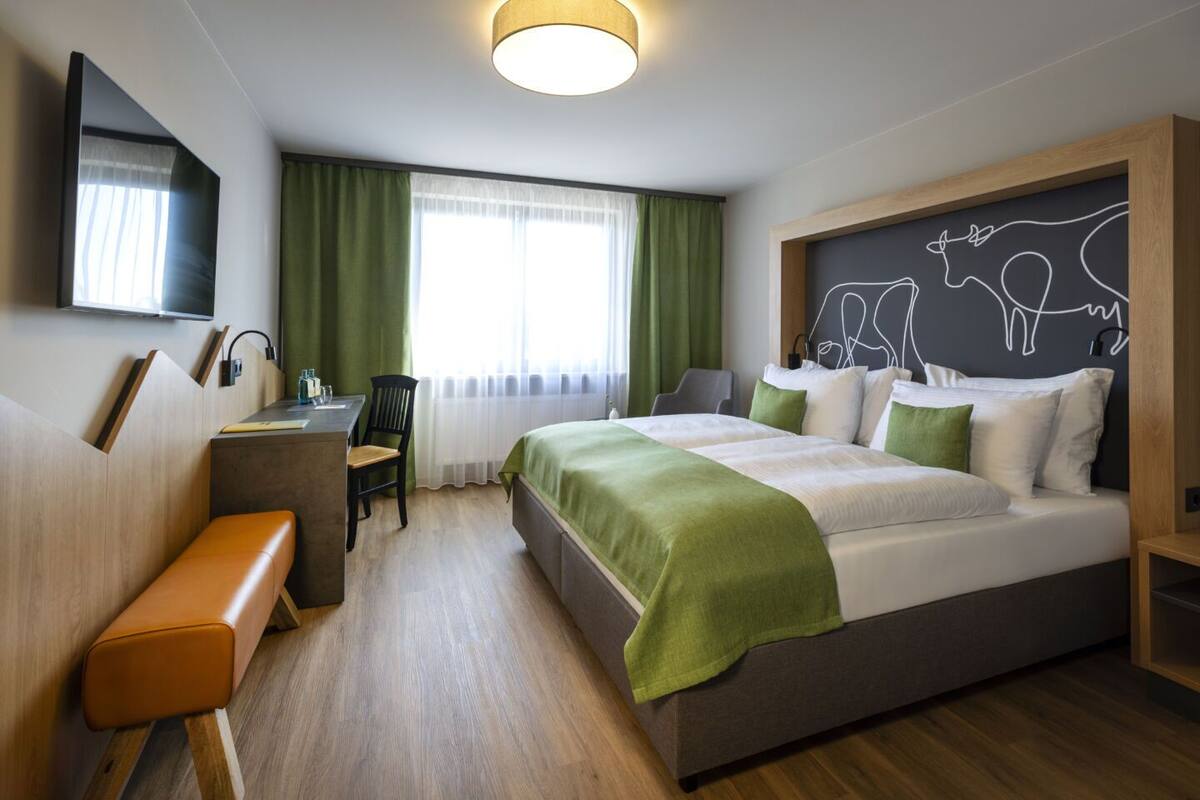 A hotel room with a bed, desk, chair, and a TV on the wall.