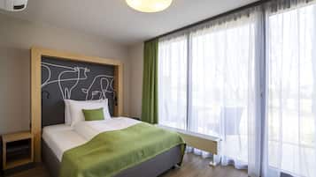 Quarto de hotel moderno com uma cama grande, cabeceira com design exclusivo, mesa de cabeceira e vista para o exterior através de cortinas leves.