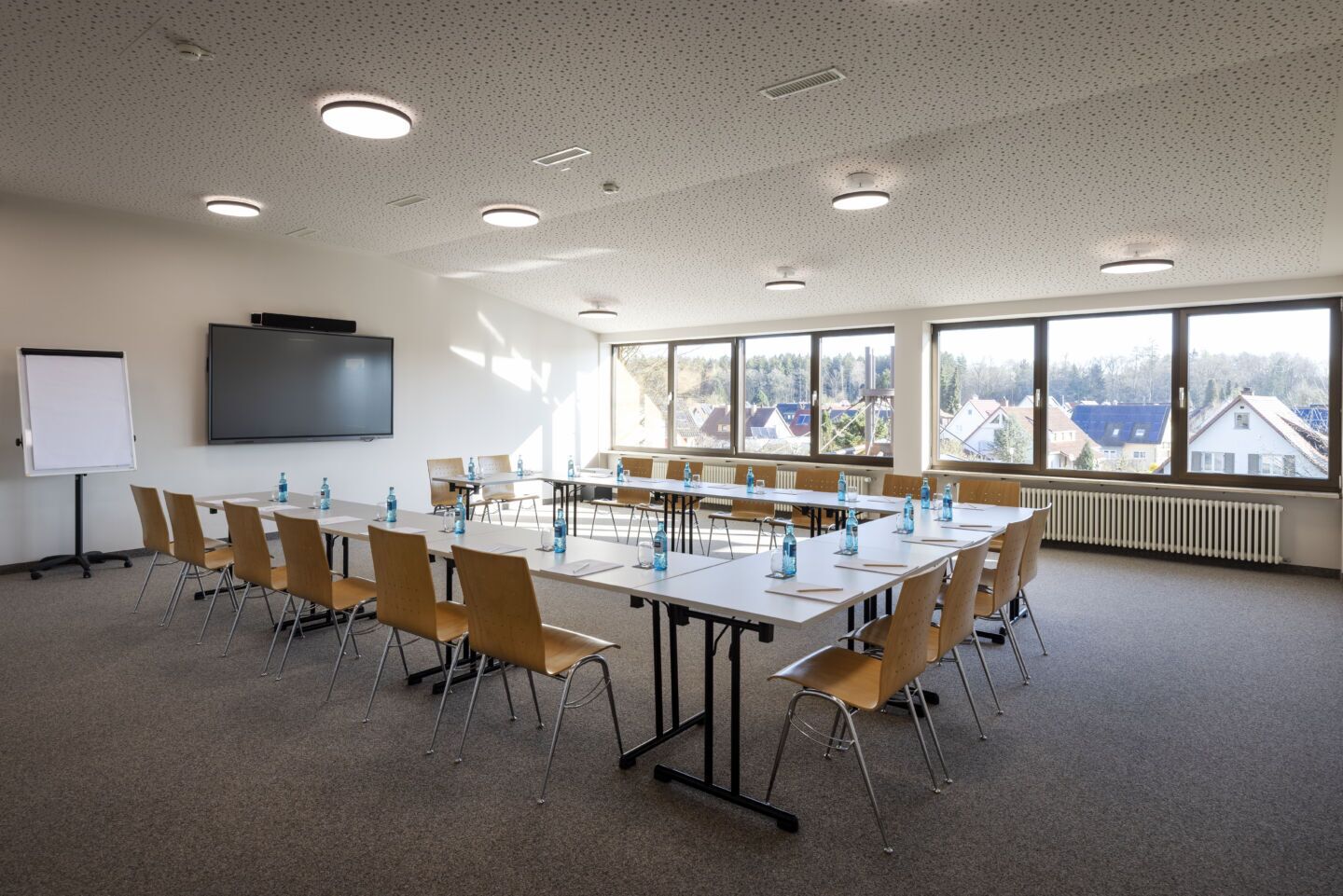 A conference room with a large table, chairs, a whiteboard, and a TV screen.