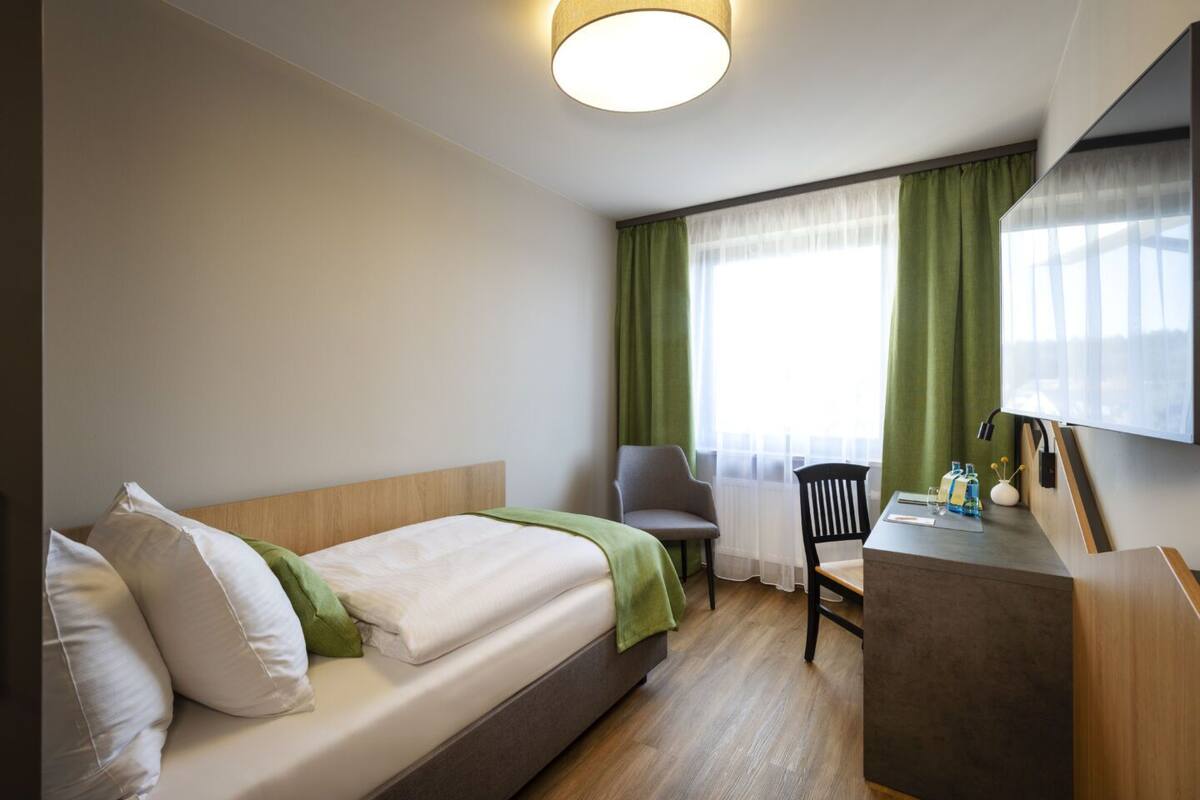 A hotel room with a bed, a desk, a chair, and a large window with curtains.