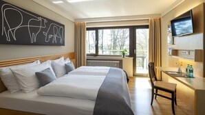 Habitación de hotel con una cama grande, un escritorio, un televisor y una ventana con vistas a árboles.
