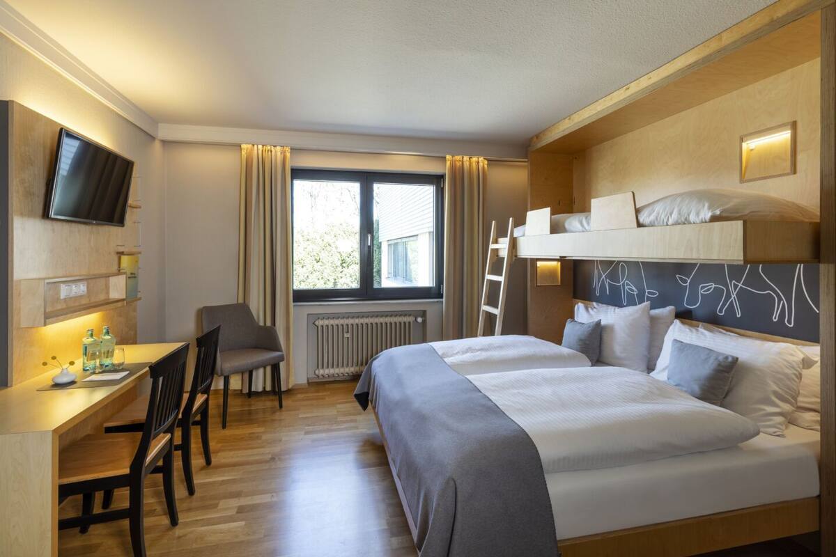 A hotel room with a bed, desk, chair, and a TV mounted on the wall.