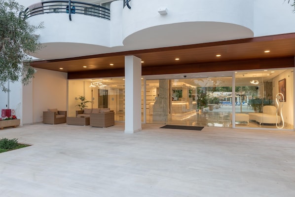 Un edificio moderno con un amplio espacio exterior, mobiliario para sentarse y una entrada de cristal que da a un espacio interior.