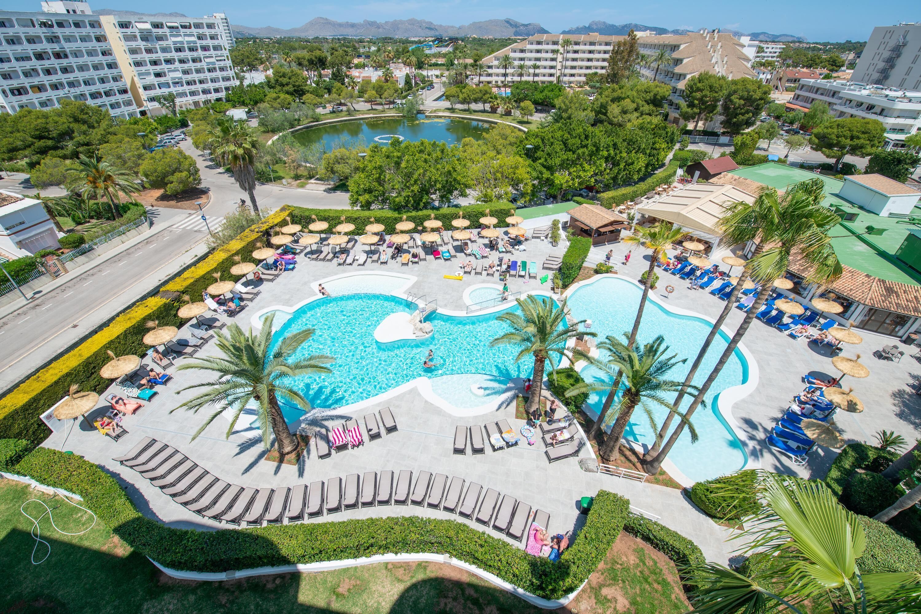 A resort with a large pool area, multiple lounge chairs, and palm trees.