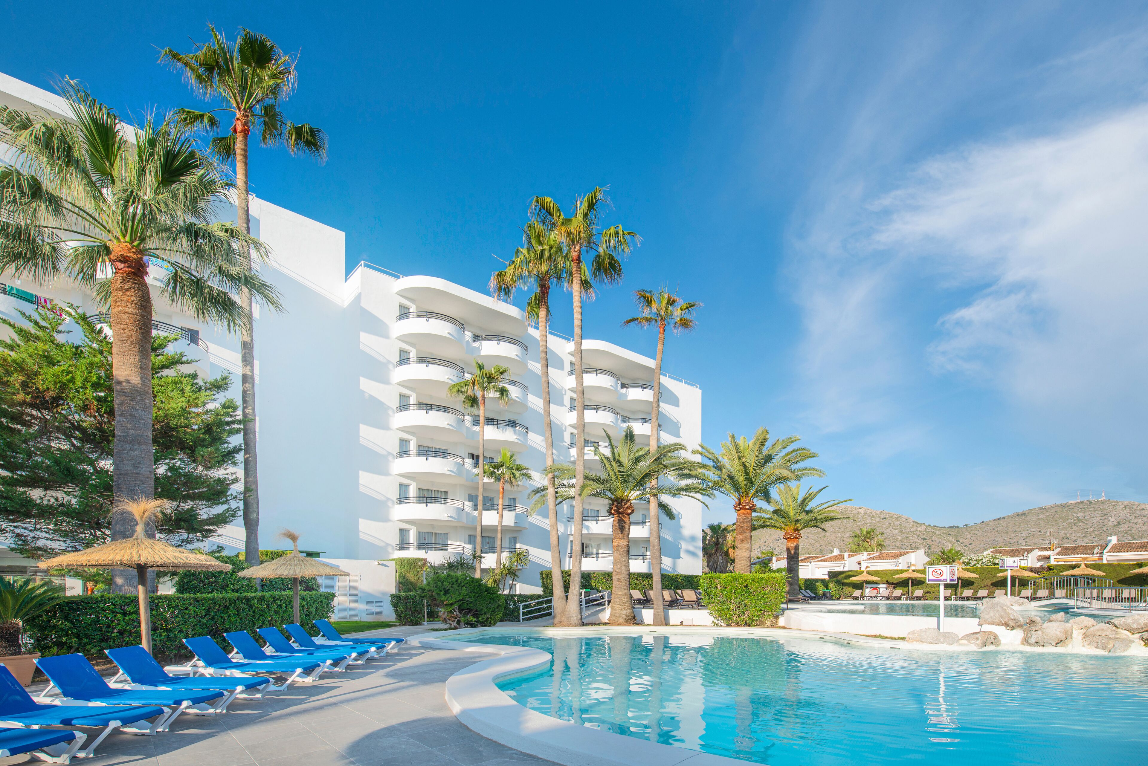 A resort with a swimming pool, palm trees, and a white building with balconies.