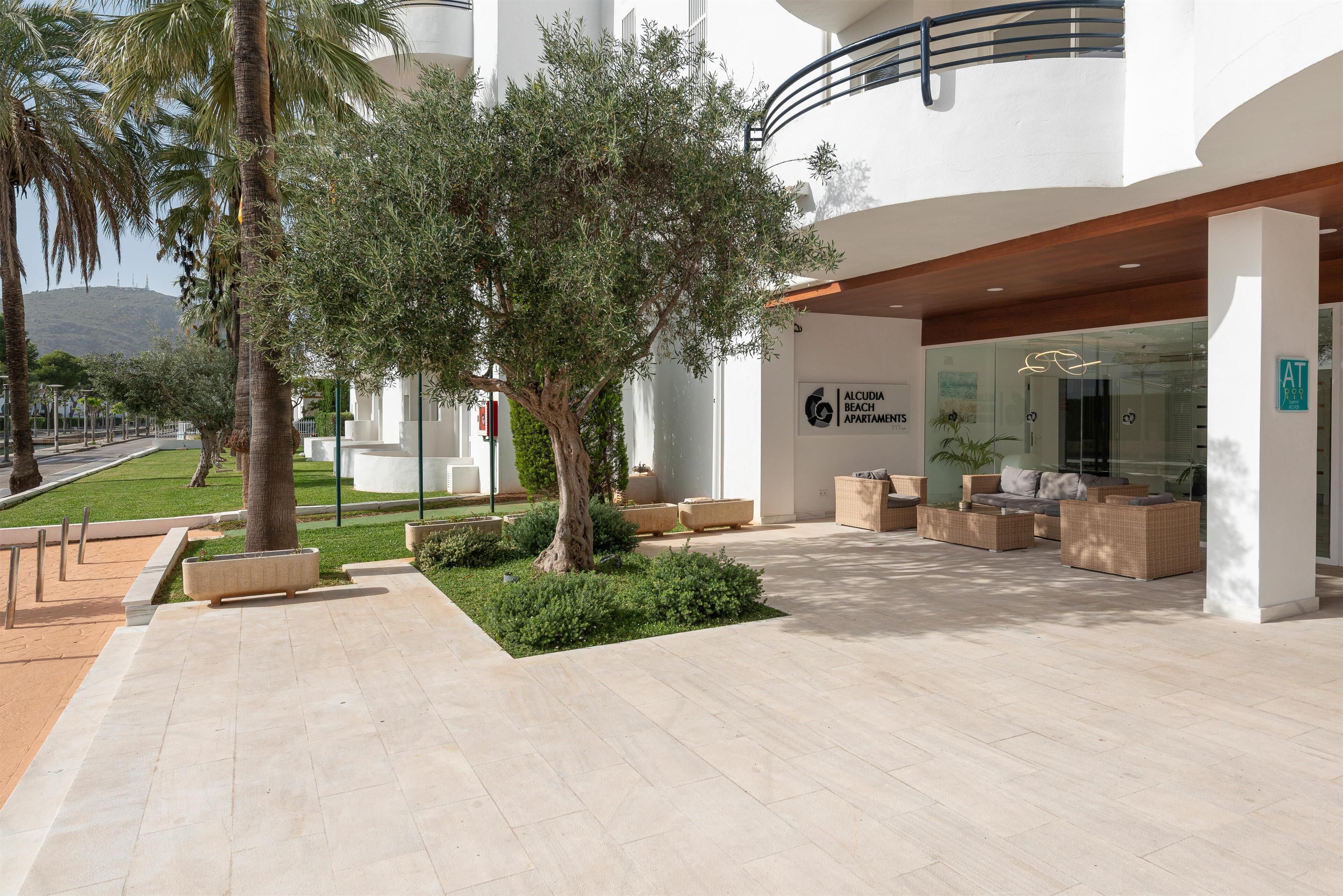 Un moderno vestíbulo de hotel con una zona de estar, un cartel de Alcudia Beach Apartments y vistas del paisaje circundante.