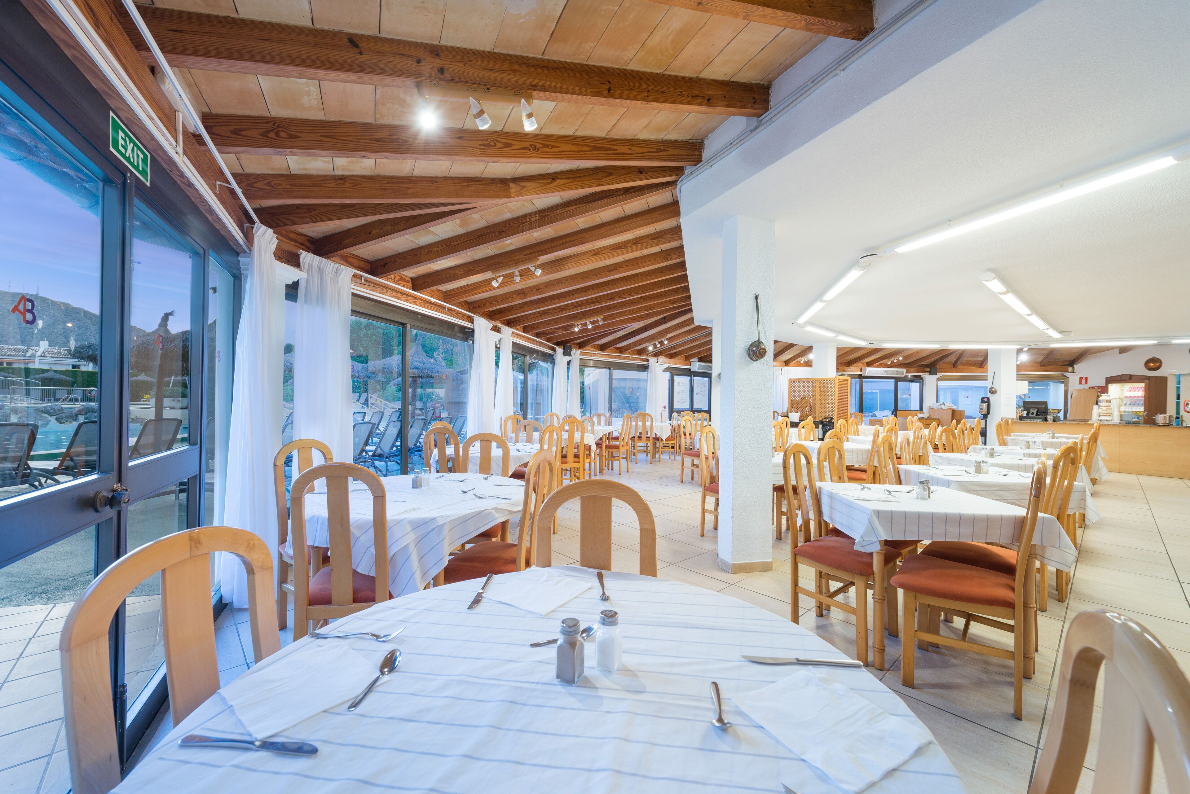 Un ristorante con travi in legno, tovaglie bianche e sedie.