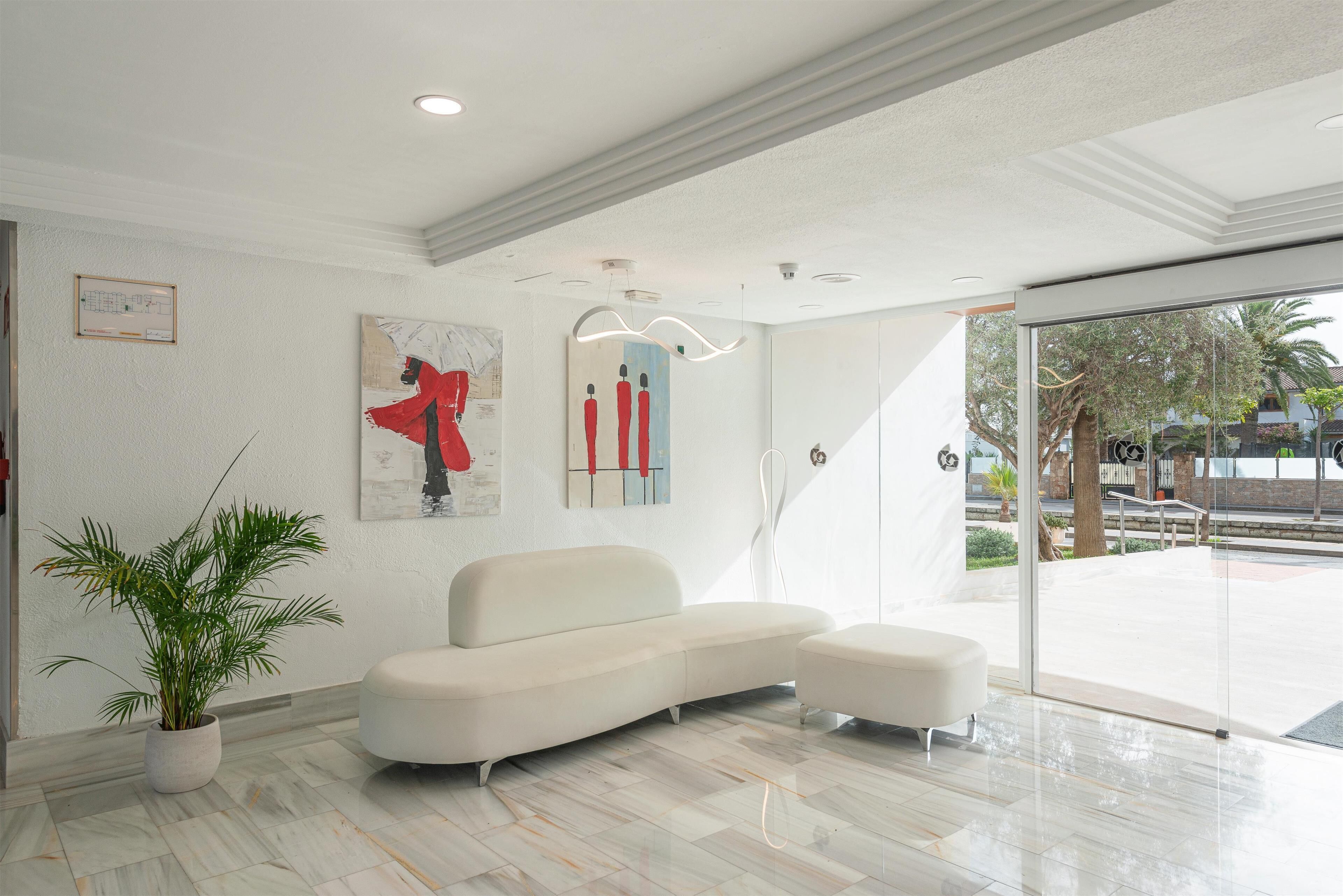 Un vestíbulo moderno con un sofá blanco, una planta en maceta y obras de arte en las paredes.