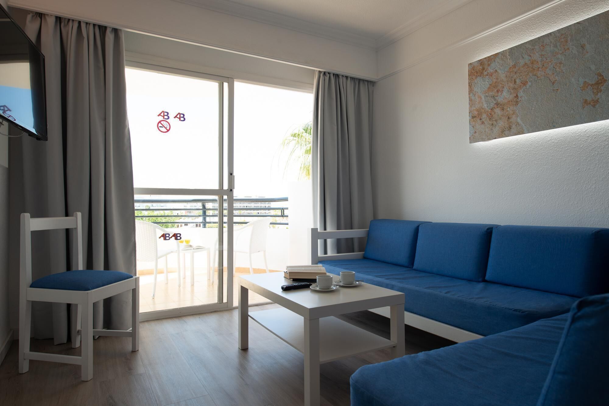 A modern living room with a blue sofa, white armchairs, a small white table, and a TV on the left.