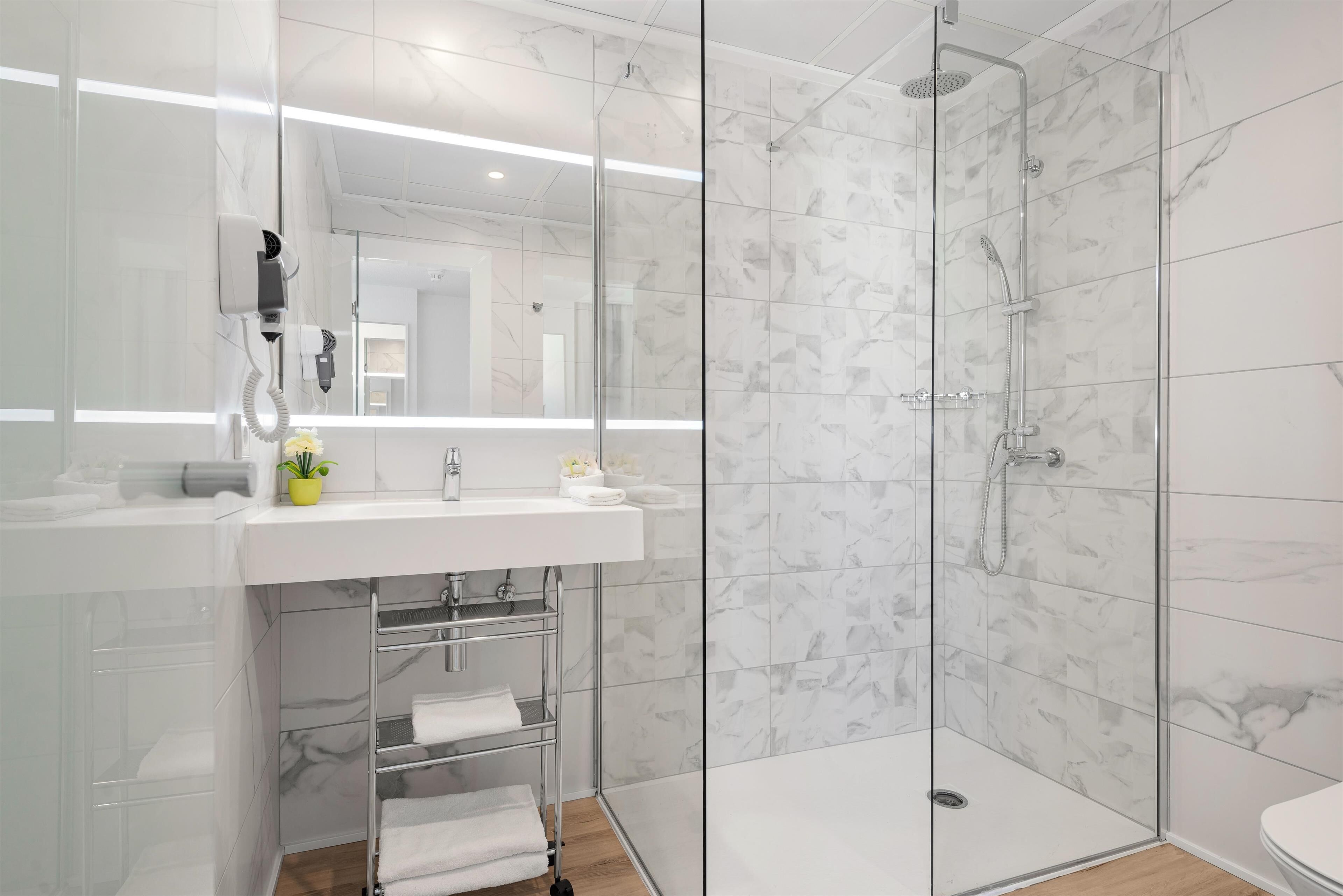 A modern bathroom with a glass-enclosed shower, a white sink with a mirror, and a towel rack.