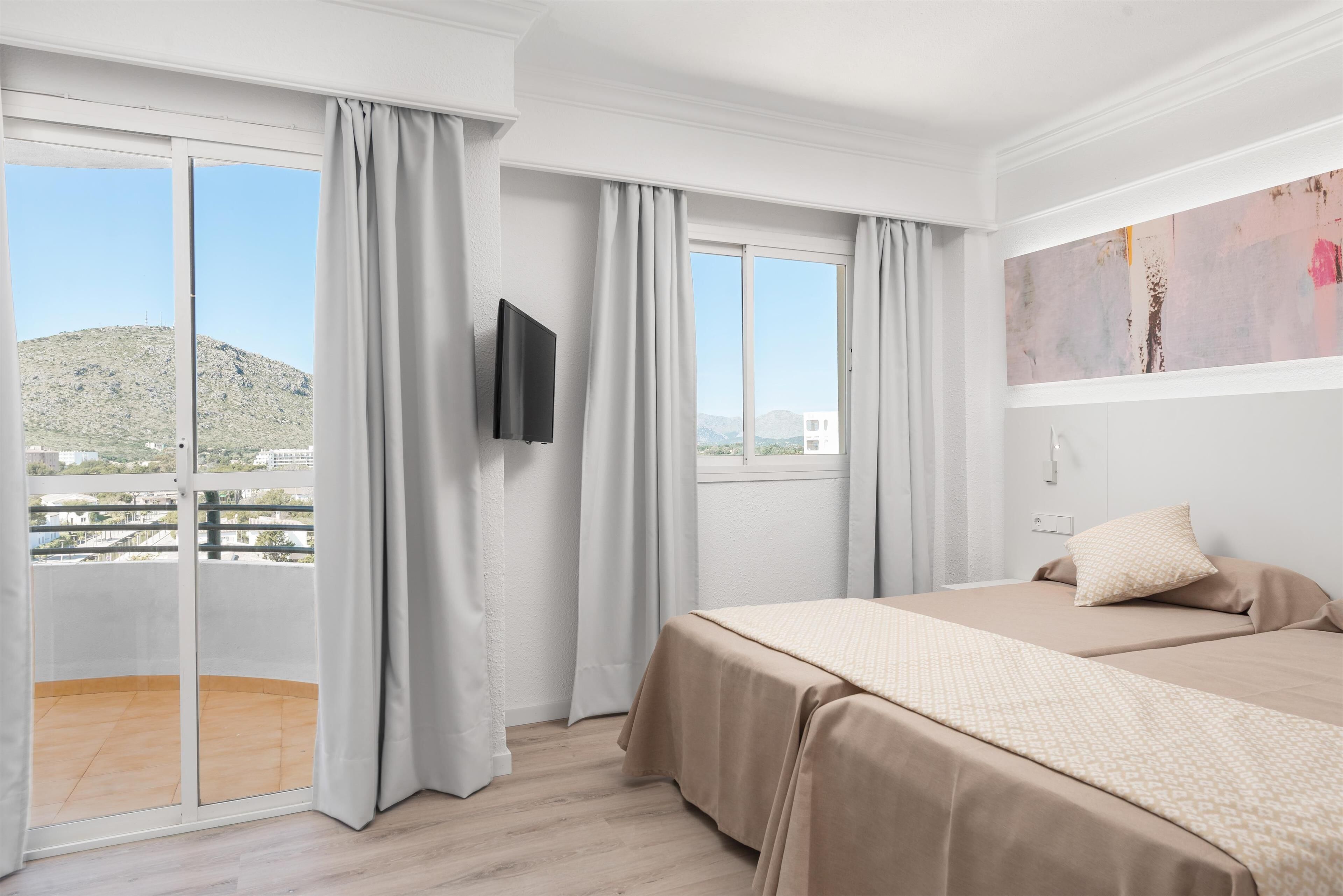 Una camera d'albergo con un balcone, un letto, una TV e un quadro appeso al muro.