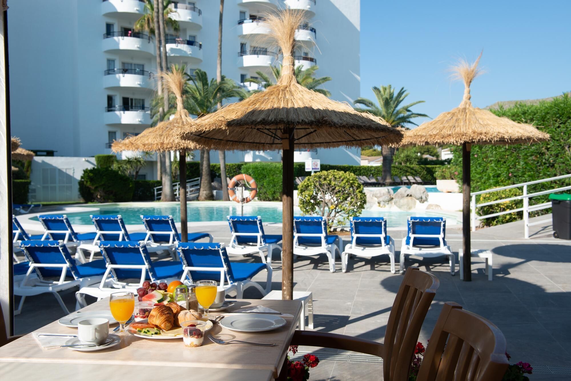 A poolside dining area with tables, chairs, and umbrellas.