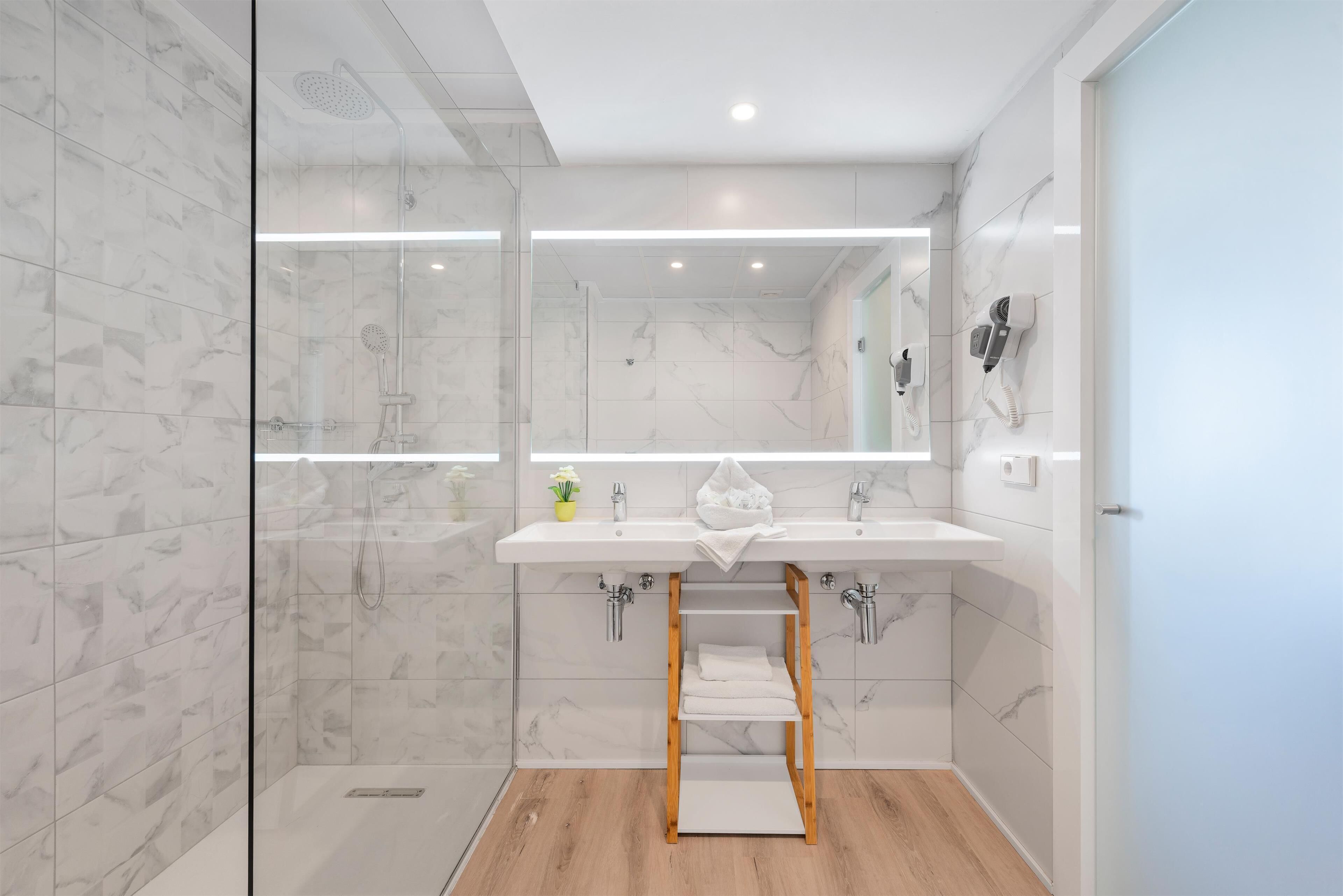 Een moderne badkamer met een douche met glazen wand, een witte wastafel met spiegel en een houten plank.