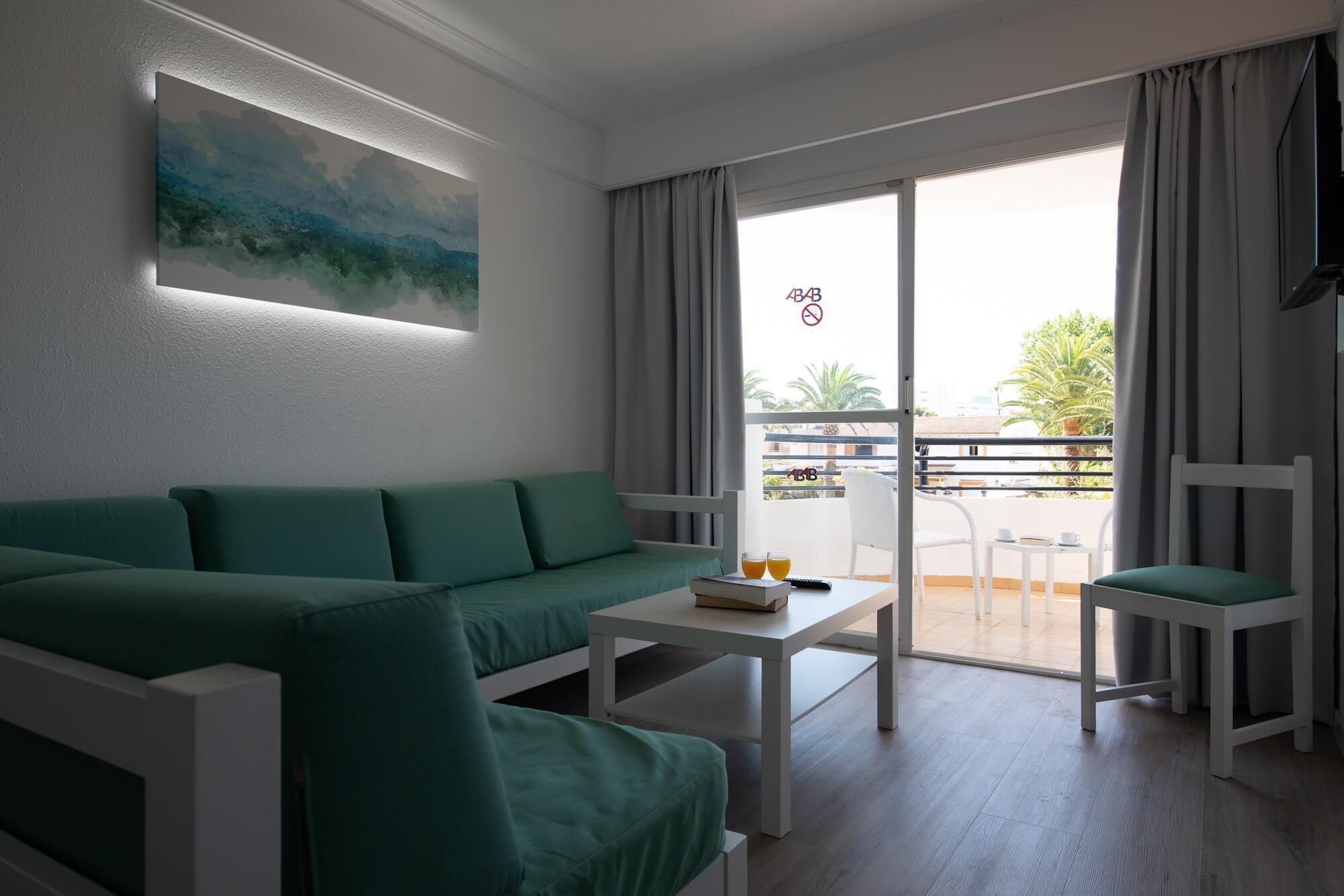 A modern living room with a green sofa, a white coffee table, and a balcony with a view of the outdoors.