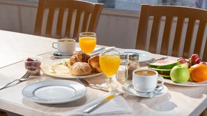 Una mesa de desayuno con cruasanes, jugo de naranja, café y fruta.