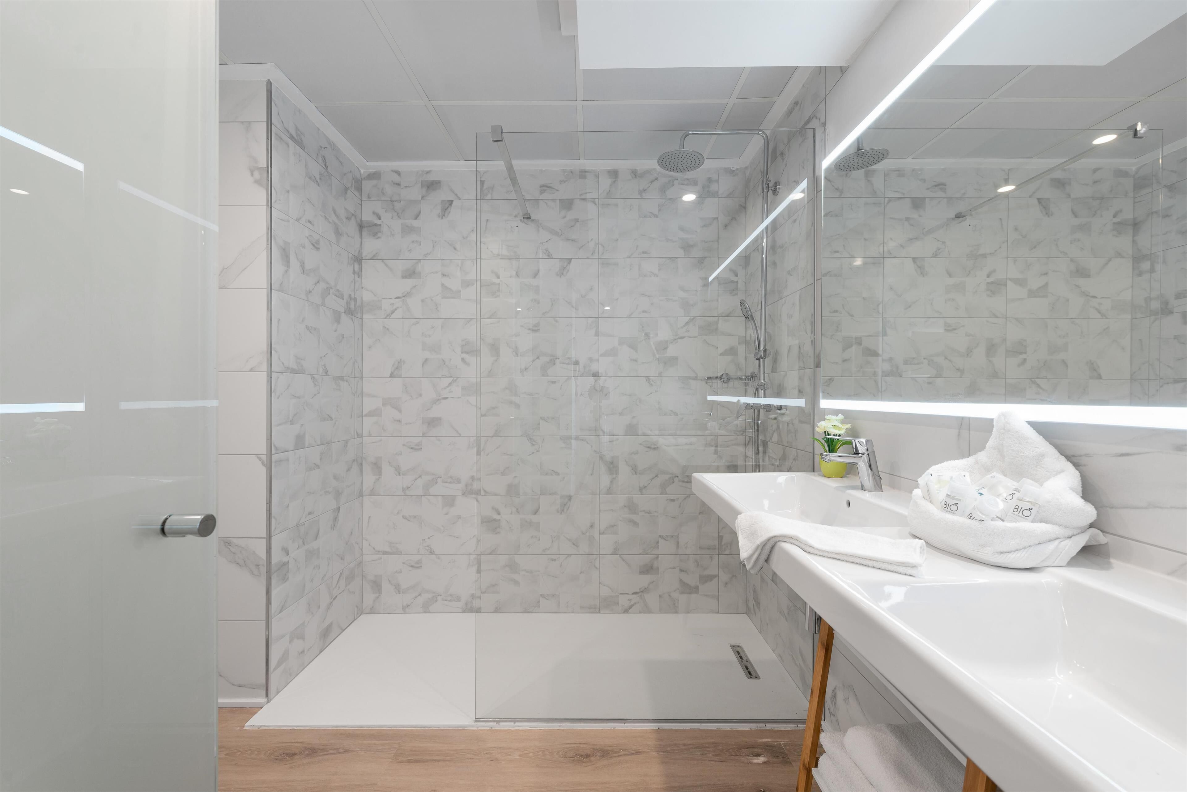 A modern bathroom with a glass shower enclosure, a white sink, and a mirror.