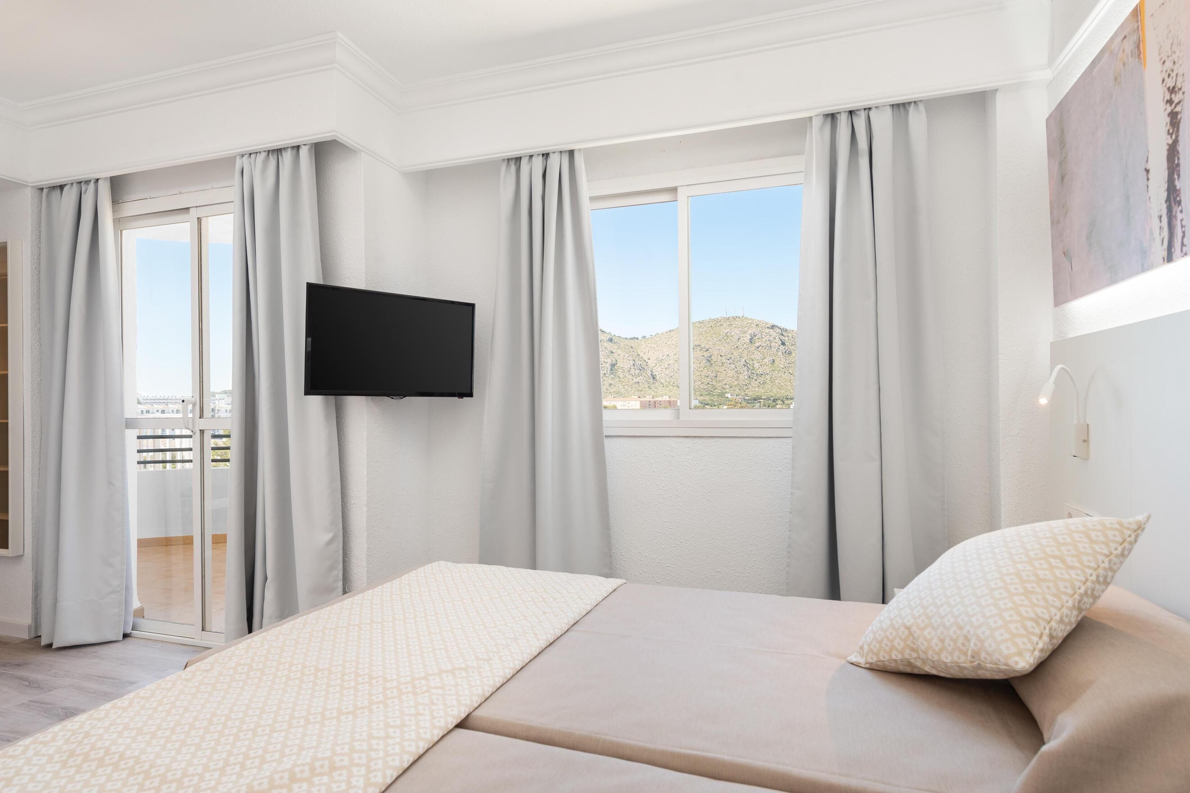 Un dormitorio con cama, televisión de pantalla plana y balcón con cortinas.