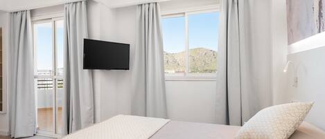 Une chambre à coucher avec un lit, un téléviseur à écran plat et un balcon avec des rideaux.
