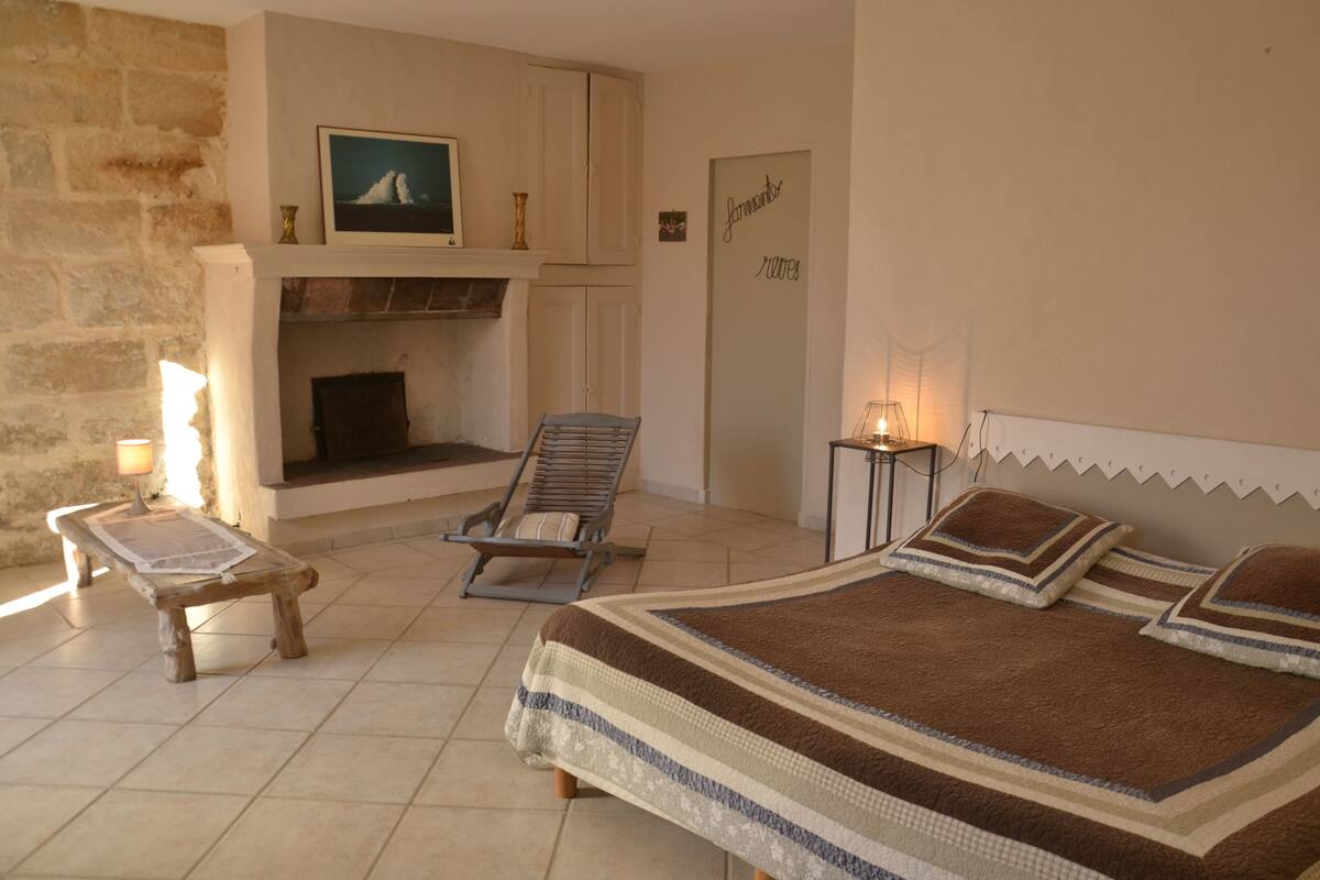 Un dormitorio con chimenea, una cama con ropa de cama a rayas, un banco de madera y una silla.