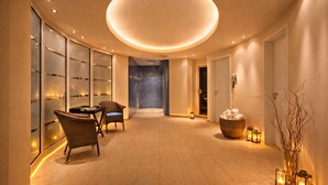 A modern, well-lit hallway with a circular ceiling light, wicker chairs, a small table, a basket of towels, and a glass wall with a view. - Hotel Sonne Rheda Wiedenbrück (Rheda-Wiedenbruck)