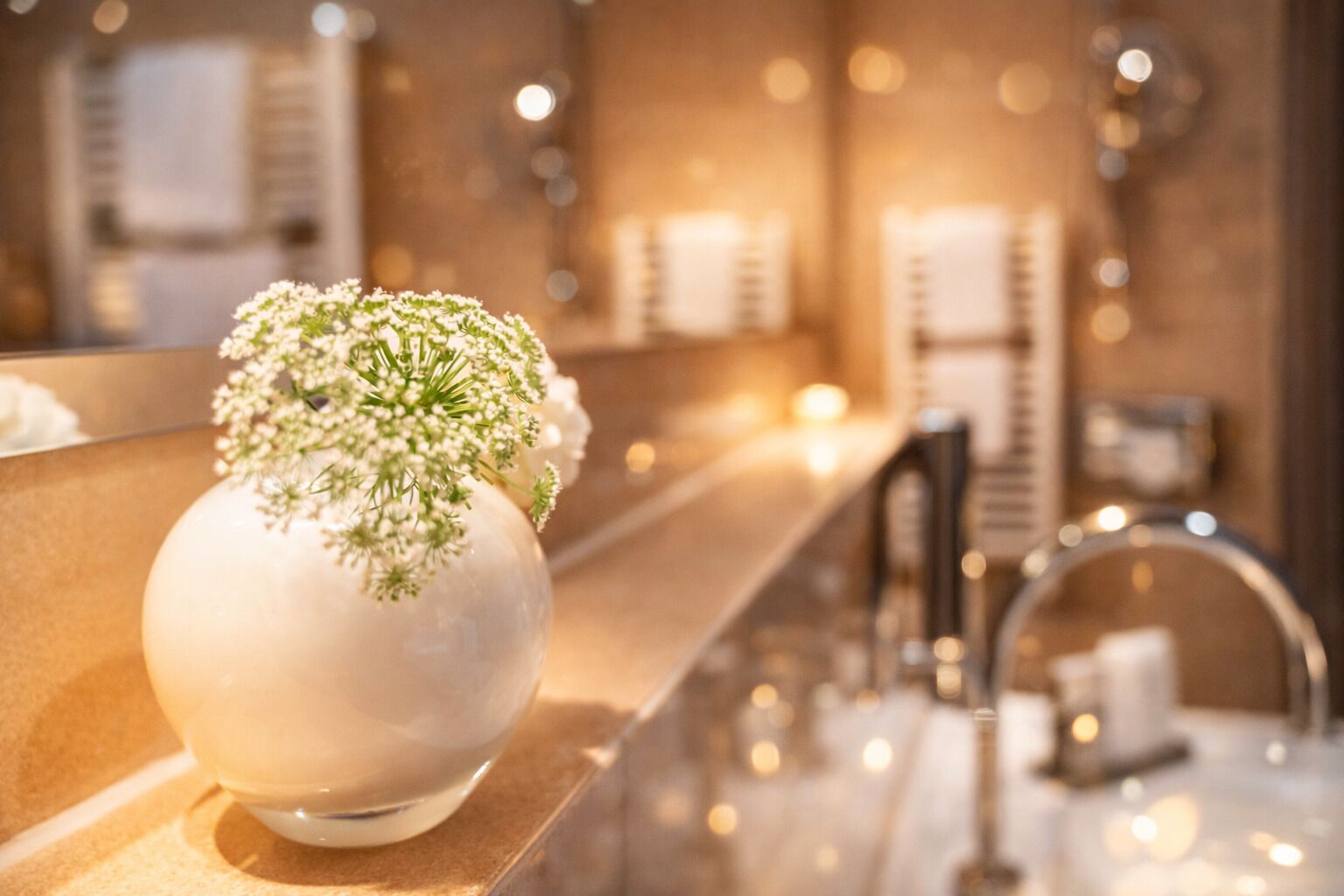A bathroom with a white vase containing white flowers on a countertop.