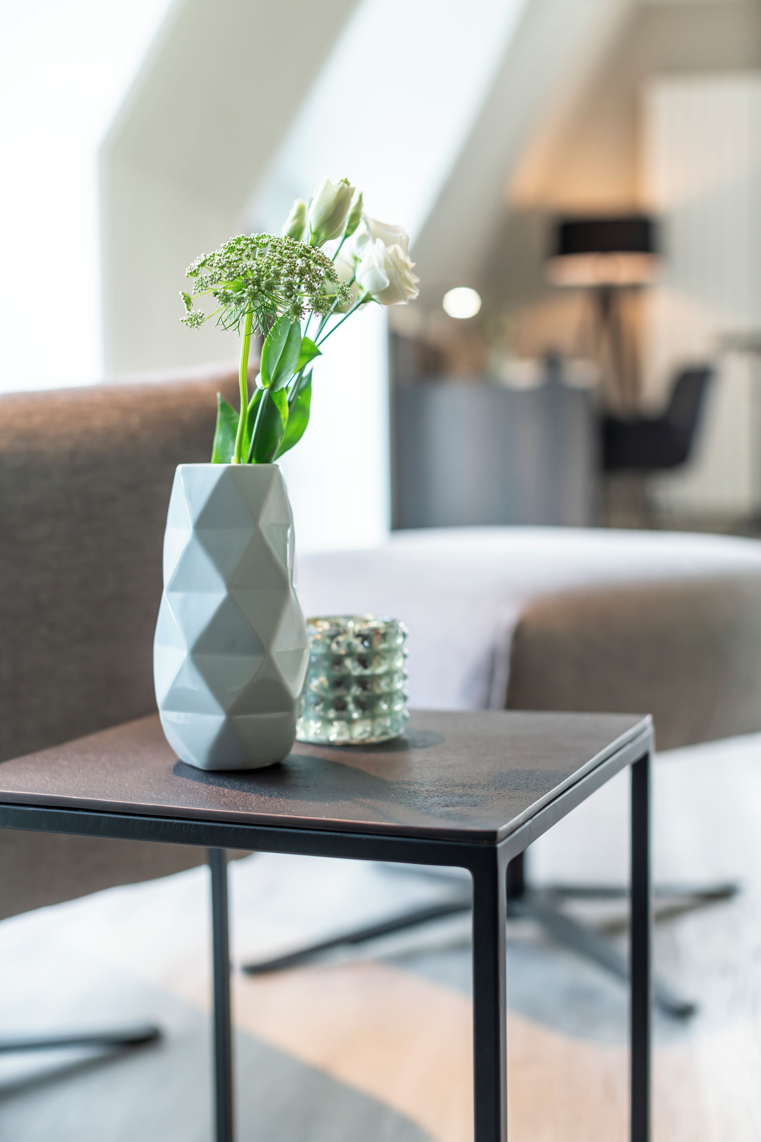 A modern living room with a geometric vase on a table, a sofa, and a lamp in the background.
