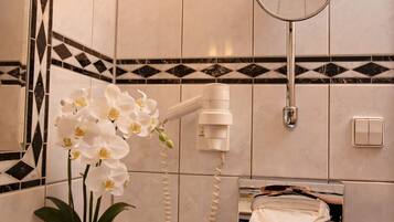 A bathroom with a shower, a towel rack, a mirror, and a potted orchid.