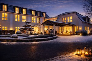 Un hotel con fachada simétrica, numerosas ventanas y un jardín nevado con un árbol central.