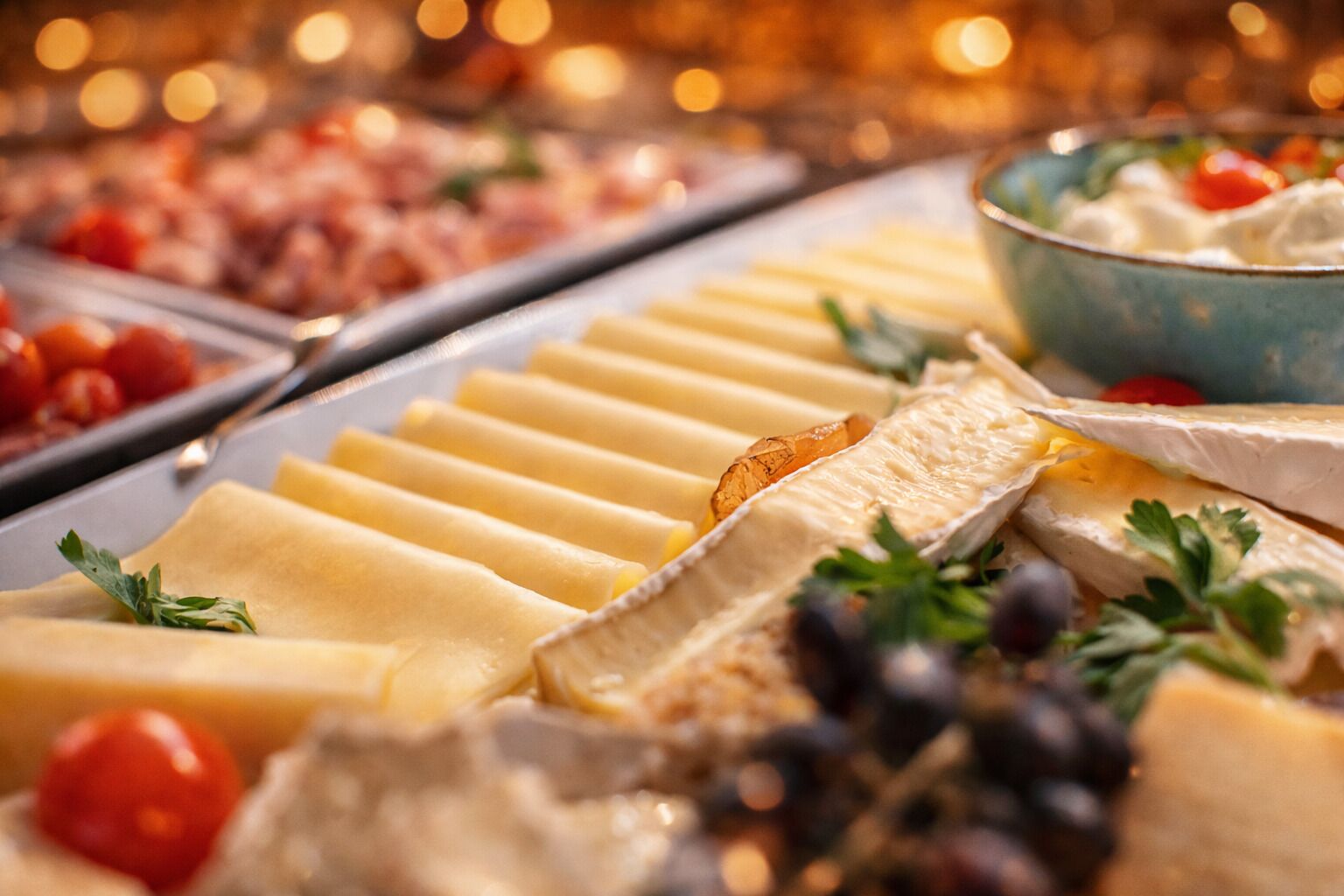 A cheese platter with various cheeses, grapes, and cherry tomatoes.