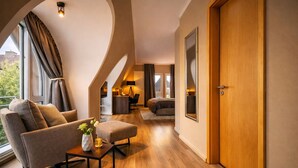 A modern living room with a sofa, ottoman, and a small table with a vase. There is a wooden door and a large mirror on the wall. - Hotel Sonne Rheda Wiedenbrück (Rheda-Wiedenbruck)