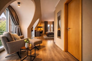 Una sala moderna con un sofá, un reposapiés y una mesita con un florero. Se ve una puerta de madera y un espejo grande en la pared.