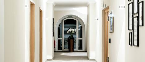 Un pasillo con paredes blancas, una puerta de madera a la izquierda y un amplio arco al final.