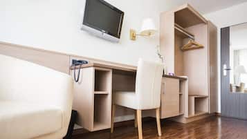 A modern hotel room with a wooden floor, a desk with a flat-screen TV, a chair, a coat rack, and a wardrobe.