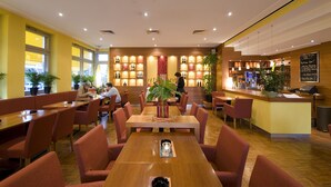 Un restaurante con mesas y sillas de madera, una zona de bar y plantas en macetas.