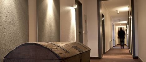 A hallway with a wooden chest, a door, and a person walking away.