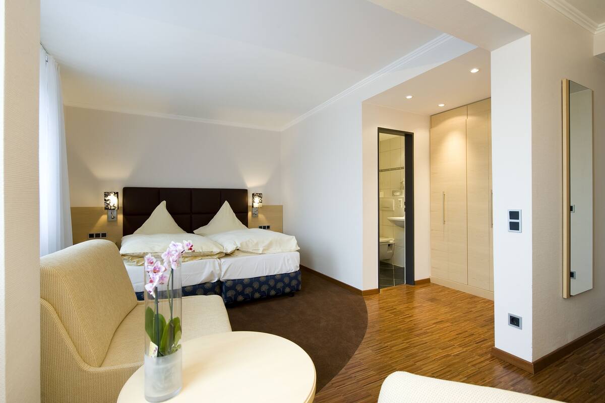 A hotel room with a bed, bedside tables, a chair, a small table with a vase of flowers, and a mirror on the wall.