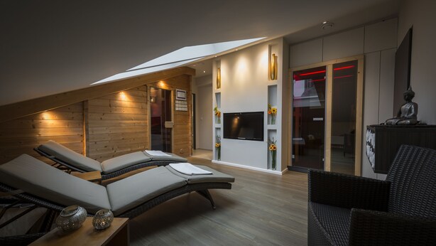 Habitación moderna y bien iluminada con techo inclinado, un televisor montado en la pared y una estatua sobre una mesa.