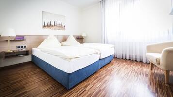 A hotel room with a double bed, a bedside table with a lamp, a chair, and a painting on the wall.