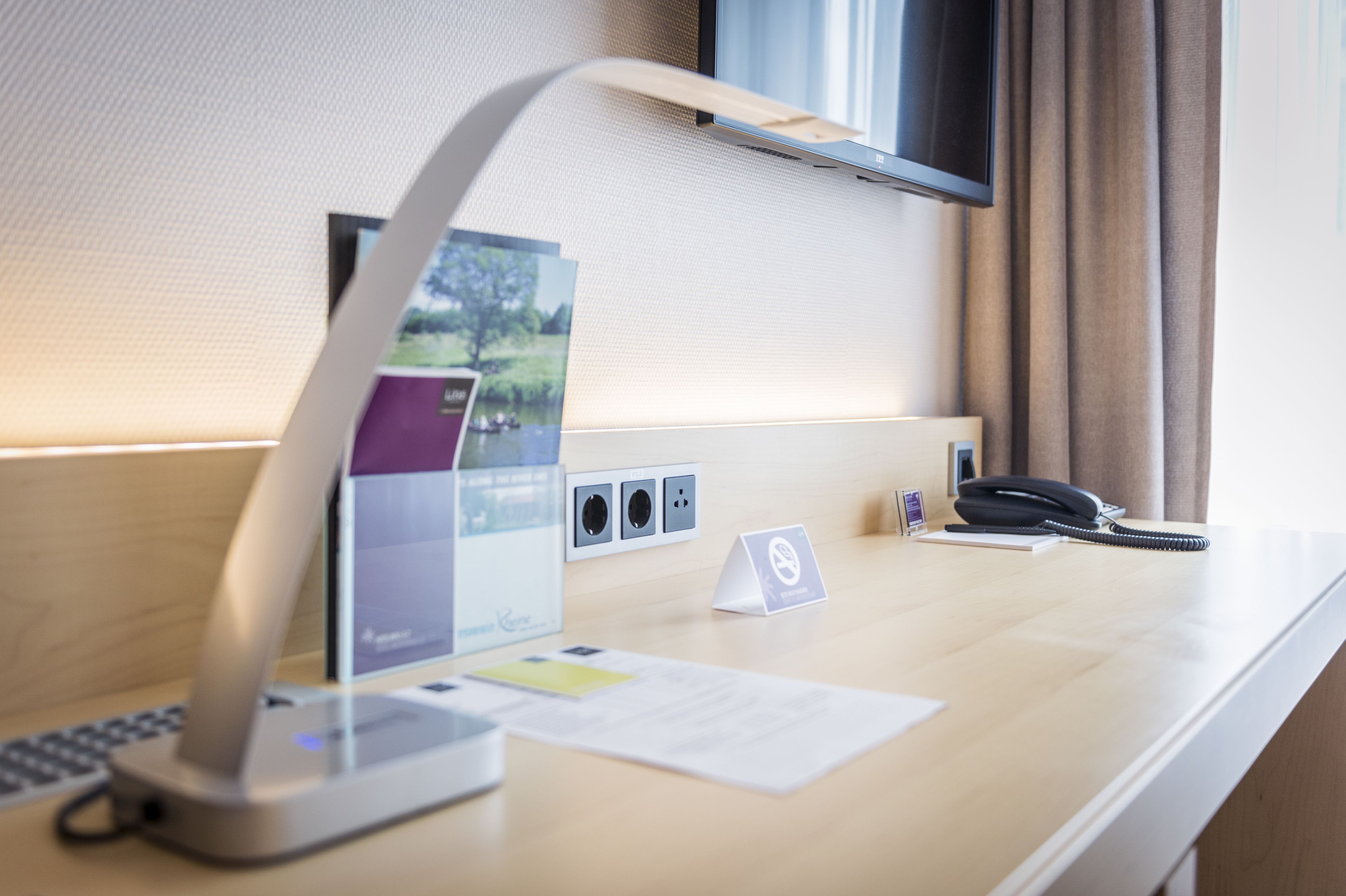 Un mostrador de hotel con una computadora portátil, un teléfono, un enchufe y una pequeña señal.