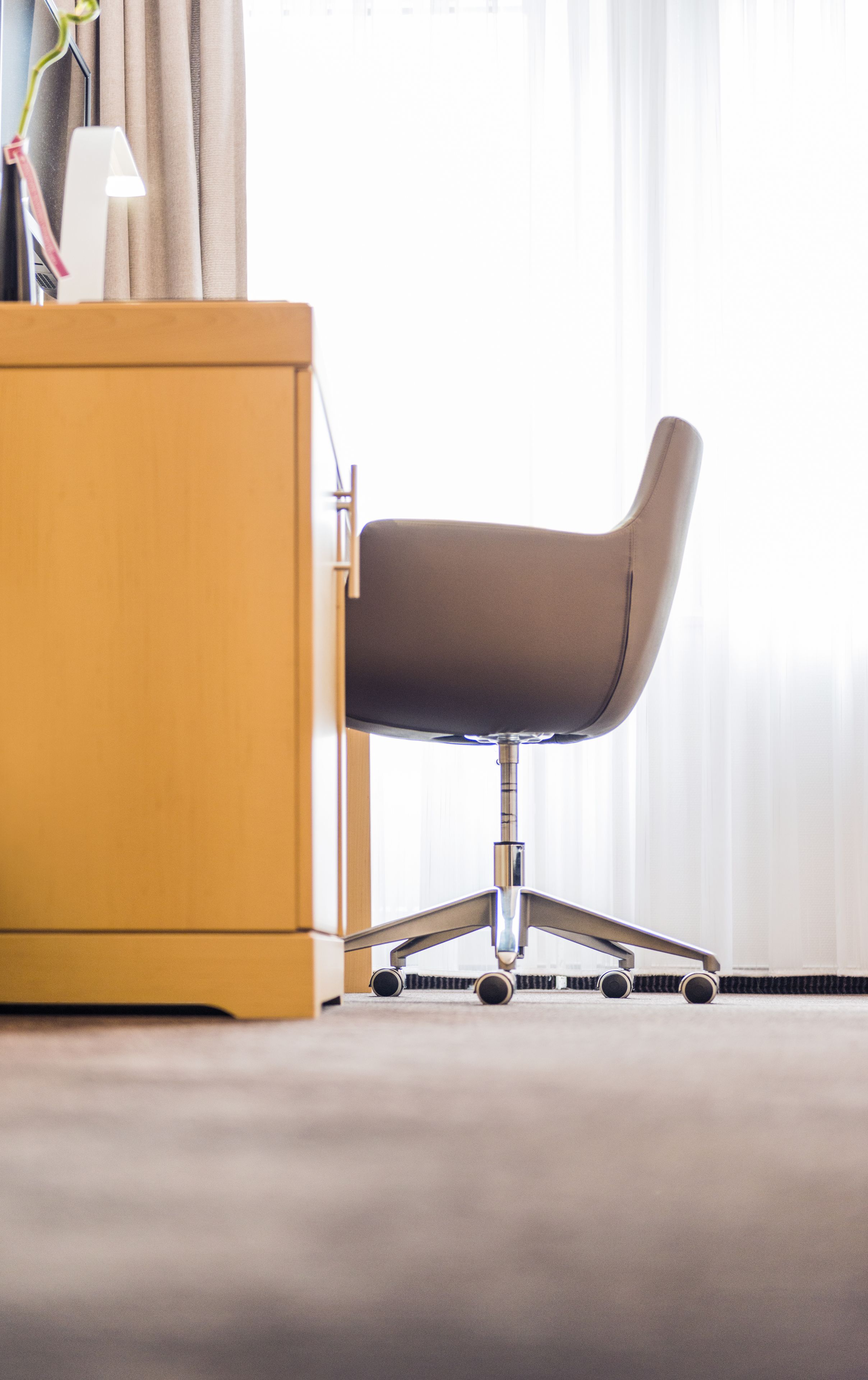 Una silla de oficina moderna con respaldo alto y base de metal, ubicada junto a un escritorio de madera con una lámpara.
